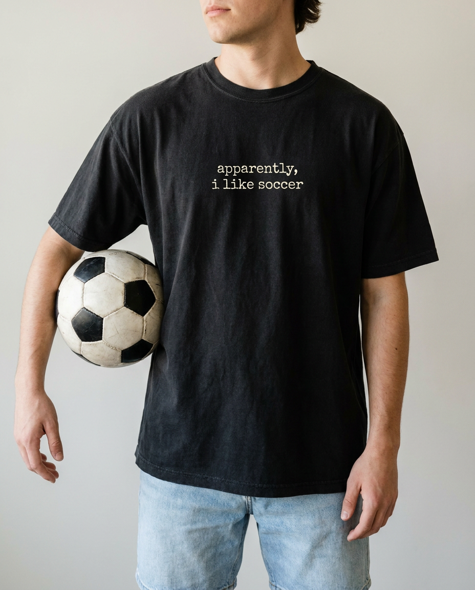 Man in black apparently i like soccer tee holding a soccer ball