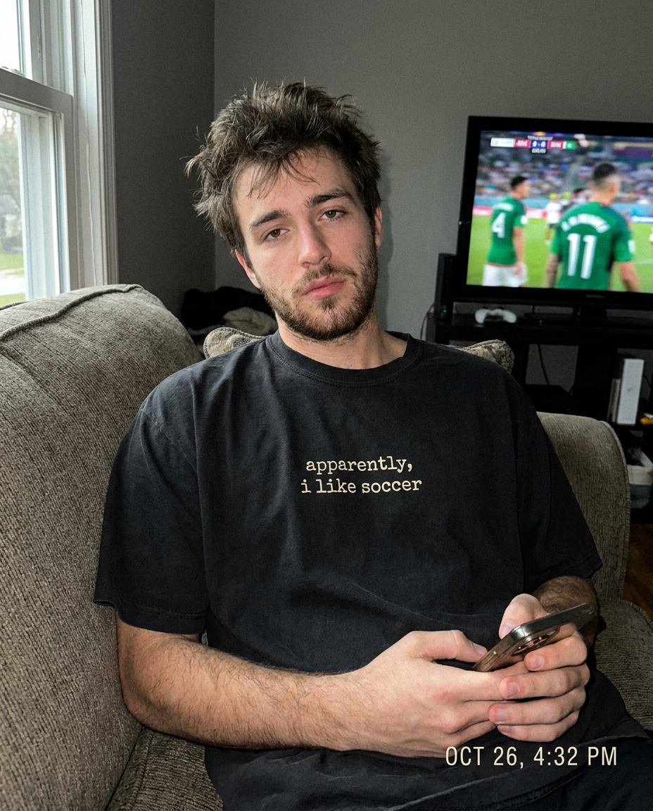 Man on couch wearing apparently i like soccer tee watching a match
