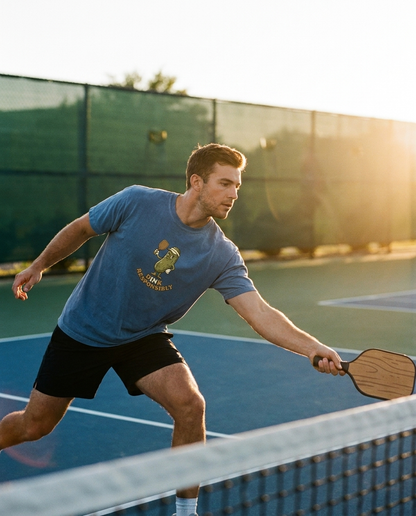 Man playing pickleball in Dink Responsibly tee at golden hour