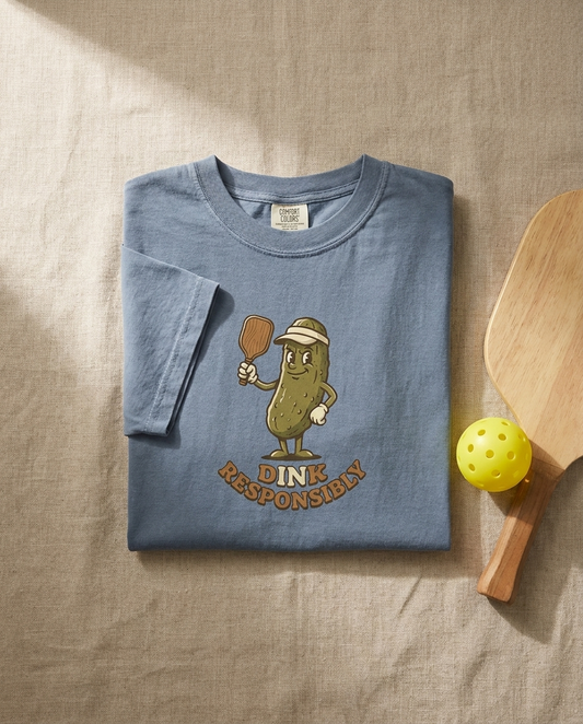 Dink Responsibly pickleball tee flat lay with paddle and ball