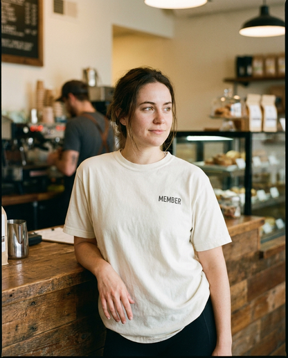 Woman at coffee shop counter in ivory Post-Run Coffee Club tee with MEMBER chest print
