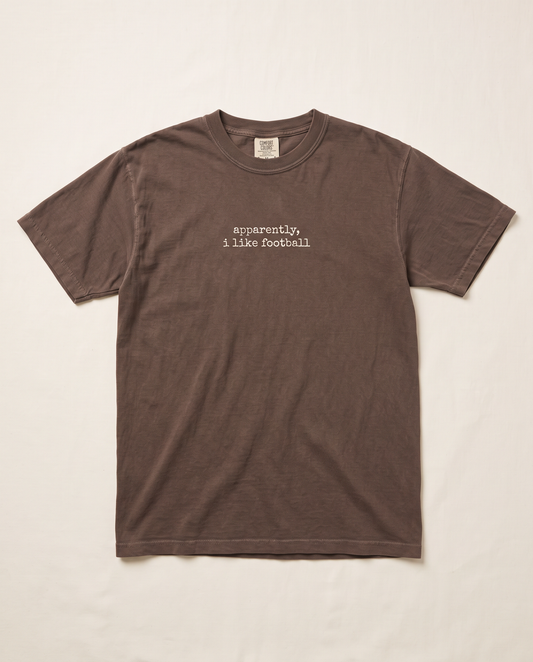 Apparently I Like Football tee — small cream chest print on espresso Comfort Colors tee, flat lay