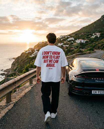 Man wearing the white tee with red back print on a coastal road at sunset